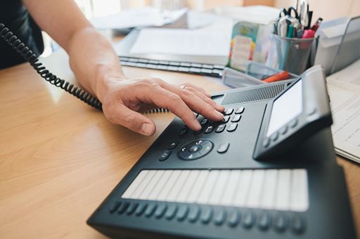 Hand Dials a Black Corded Phone in Office